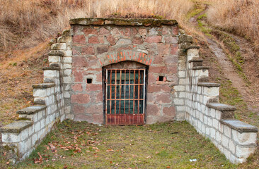 Metal lattice wine cellar door on the hillside between an old brick wall