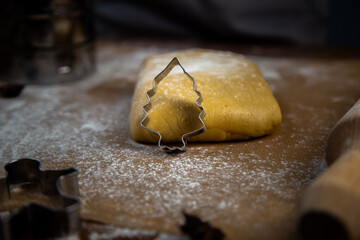 A cookie cutter in the form of a Christmas tree leaned on the dough, flour, other cookie cutters and a rolling pin for dough can be seen in the background. High quality photo
