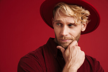White bearded man wearing hat holding his chin while looking aside