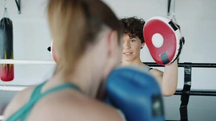 Female boxing coach is motivating student young woman training punches with gloves insing ring in gym. Youth and active lifestyle concept. - Powered by Adobe