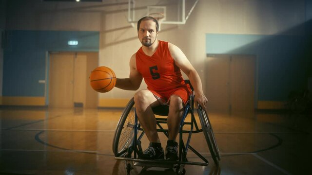 Portrait of Handsome Wheelchair Basketball Player Wearing Red Shirt Dribbling Ball, Looking at Camera and Shooting it Perfectly. Determined Person with Disability who is Gonna Win and be Champion