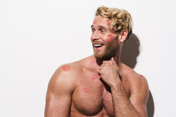 White shirtless man with lipstick marks smiling and looking aside