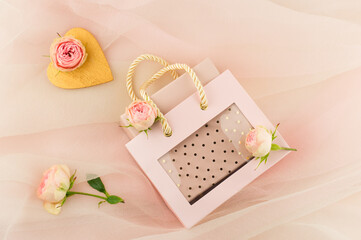 Valentine's Holiday. Beautiful gift box in a festive bag on a pink pastel background veil with buds of live roses. A gift with love.