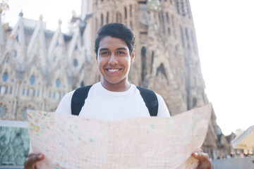 Half length portrait of cheerful Latin tourist with paper location map smiling at camera during...