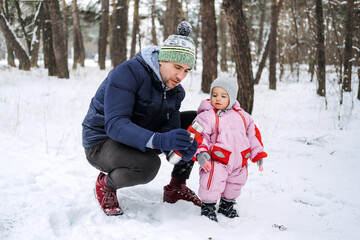Fototapeta na wymiar Outdoor family activities for happy winter holidays. Happy father and mother playing with little baby toddler girl daughter in winter park, forest. Happy family on winter weekend, Christmas holidays
