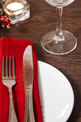 Christmas table setting. Plate and cutlery on red napkin. Candles burning on table on Christmas Eve. Preparing for festive dinner.