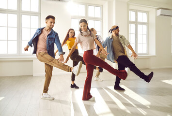 Professional dance crew having fun. Cheerful young people enjoying dance class with coach. Group of happy dancers in trendy casual wear dancing together in sun light in modern dance hall. Lens flare