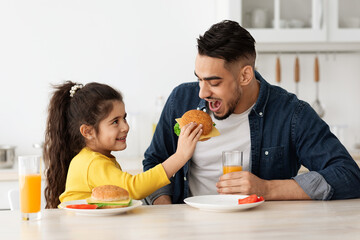 Caring Little Daughter Feeding Arab Dad With Sandwich In Kitchen