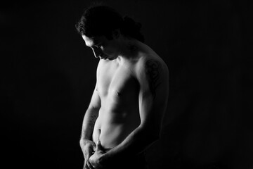 Fototapeta na wymiar black and white low key portrait of shirtless man looking at down black background