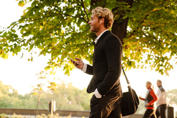 Blonde man using earphones and mobile phone in summer park