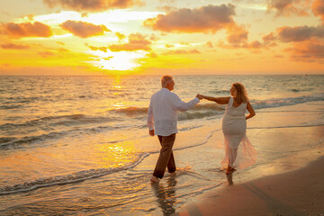 Couple enjoy their walk along beach together after elopement ceremony with sunset in background for these silhouette images.