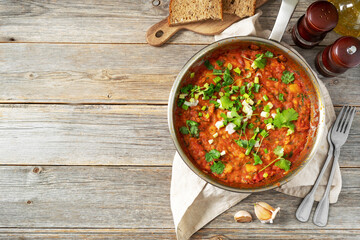 Homemade vegetarian stew with beans, vegetables and cilantro in a frying pan on a gray wooden culinary background. Top view