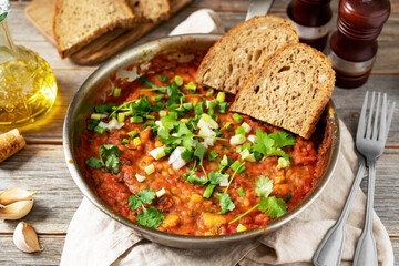 Homemade vegetarian stew with beans, vegetables and cilantro in a frying pan on a gray wooden culinary background close-up