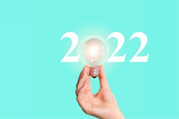 Businessman holding light bulb with year 2022 plans on a background.