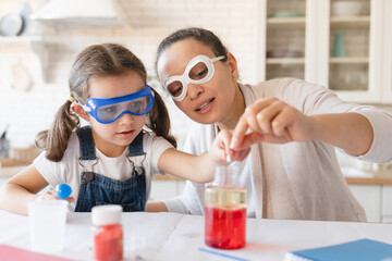 Playful mother and little daughter girl in protective wear having fun playing with chemistry lab game together. Scientific tests experiments at home for school project homework.