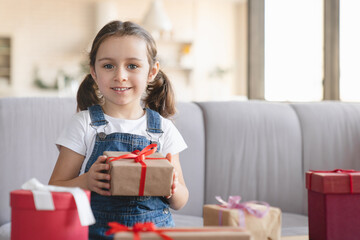 Cheerful caucasian small girl kid child daughter holding gift boxes presents, opening unwrapping...