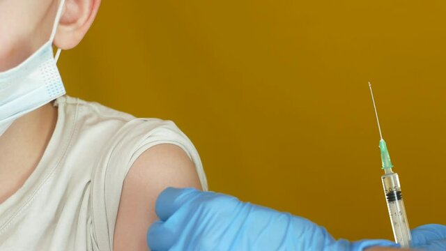 Close-up shot of a 7-8 year old Caucasian boy being vaccinated in the shoulder at the clinic. Vaccination against coronavirus Covid-19 in children and adolescents theme.Medicine in gloves