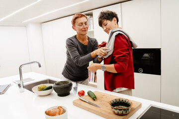 Mature lesbian couple smiling while cooking together in kitchen