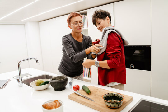 Mature Lesbian Couple Smiling While Cooking Together In Kitchen