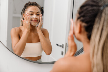 Black woman cleaning her face with lotion at bathroom
