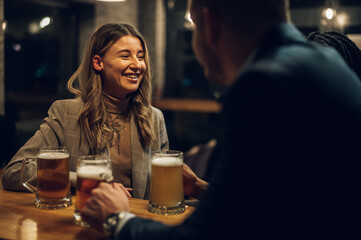 Cheerful colleagues drinking beer in the bar together after work and using a tablet