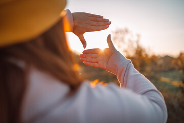 Close up of female hands making frame gesture with sunrise on an autumn meadow at sunset with sun....