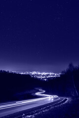 Starry sky above city lights and light trails. Night photography, toned in trendy Color Of The Year 2022 Very Peri