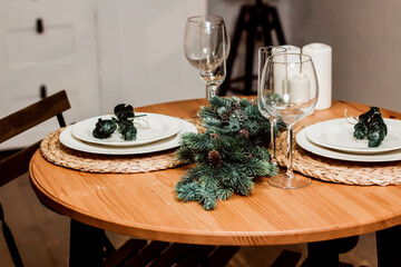 Round table decorated for Christmas and New Year. Christmas tree twigs on the table. Plates and wine glasses on the table. Kitchen set and flowers on the background. Christmas content.