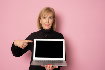 Senior woman showing laptop computer screen isolated over pink background.