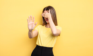 pretty caucasian woman covering face with hand and putting other hand up front to stop camera,...