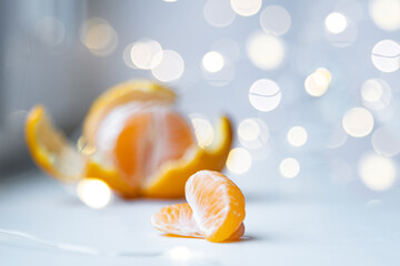 Partially peeled tangerine and tangerine slices, on a light background, with a bokhe of lights. Attributes of Christmas and New Year. Merry Christmas and Happy New Year.