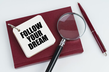 On a white surface lies a red notebook and a pen, in the white notebook the inscription - FOLLOW...