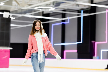 happy woman in ear muffs and pink sweater on ice rink.