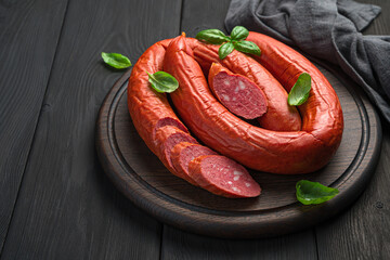 Smoked, Cracow sausage with basil on a cutting board on a dark background.