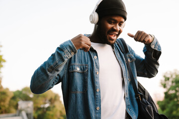 Black man listening music with headphones while walking in park