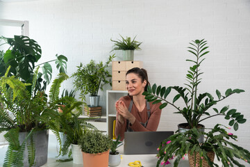 Young happy successful woman florist in her flowershop surrounded with flowers in flowerpots working job she love as small business owner.