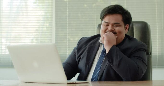 Asian business man which has a fat figure and funny personality, wearing a suit using a laptop in the office. He was hopeful and felt that he had an advantage and superior to the competition.