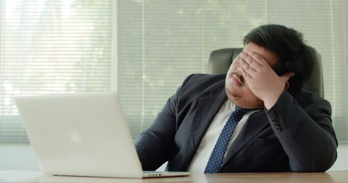 Asian business man which has a fat figure and funny personality, wearing a suit like an executive or a manager using a laptop in the office,feeling stressed and anxious about business.