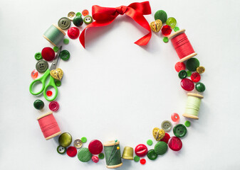 Christmas wreath made of buttons, threads, pins, scissors, thimble red, green and gold color. White background. Copy space