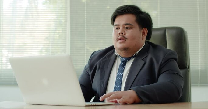 Asian business man which has a fat figure and funny personality, wearing a suit like an executive or a manager using a laptop in the office. The next time he was surprised at what had happened.