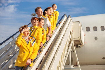 Cheerful airline workers standing on airplane stairs under blue sky