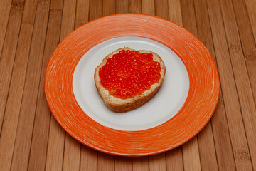 sandwich with red caviar lying on an orange plate on a wooden background