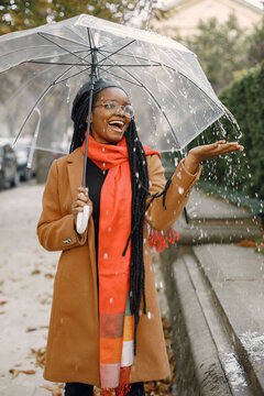 Young Black Woman In A Coat Standing Under A Transparent Umbrella Outside