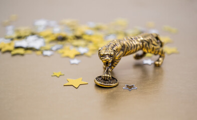 A bronze figure of a tiger with a coin - the symbol of the Chinese new year 2022 on a background of golden stars, copy space. Wishes of good luck, financial well-being and wealth