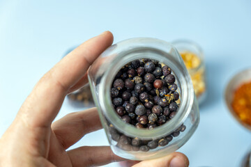 Close-up, a man holding a jar with dry useful herb for brewing. Juniper berry jar