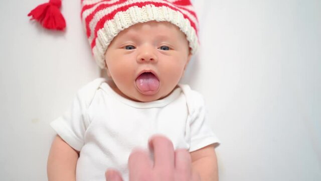 hand touches face of cute little kid in cap of Christmas elf or gnome.baby santa