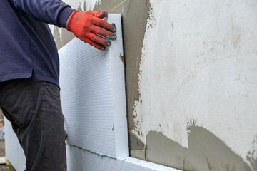 Construction worker installing styrofoam insulation sheets on house facade wall for thermal...