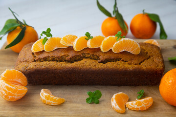 Vegan tangerine sponge cake with mandarin orange wedges on a wooden board.