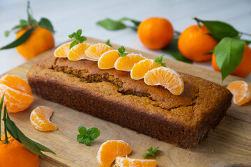 Vegan tangerine sponge cake with mandarin orange wedges on a wooden board.
