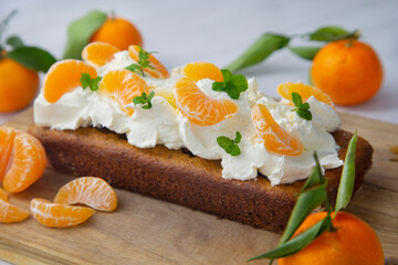Vegan tangerine sponge cake with a giant frosting and mandarin orange wedges on a wooden board.